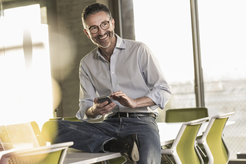Happy Mature Businessman With Cell Phone In Office - Cesanto Assessoria Empresarial | Escritório de Contabilidade na Zona Sul - SP